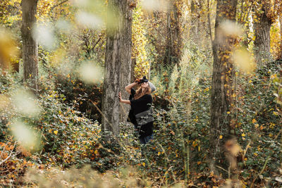 Woman photographing in forest during autumn