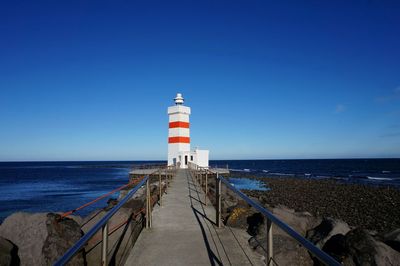 Calm blue sea with lighthouse in distance against clear sky
