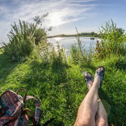 Low section of man relaxing on grass against sky