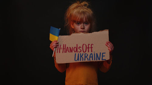 Portrait of smiling young woman holding paper against black background