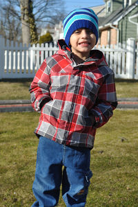 Portrait of smiling boy with hands in pockets standing on grassy field at back yard