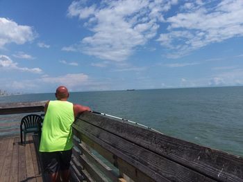 Rear view of man standing on railing against sea