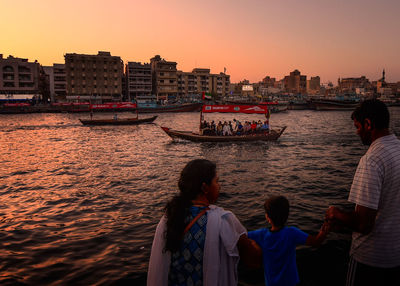 Rear view of people on boat in city at sunset