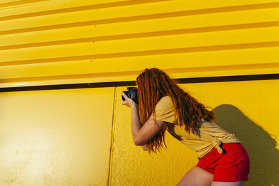Side view of woman wearing sunglasses standing against yellow wall