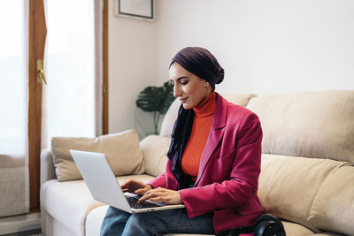 Young woman using laptop while sitting on sofa at home