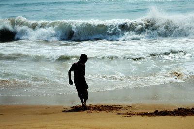 Full length rear view of boy playing on shore at beach