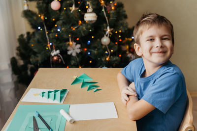 Smiling child making christmas card. glue the prepared parts of the christmas tree on the card sheet