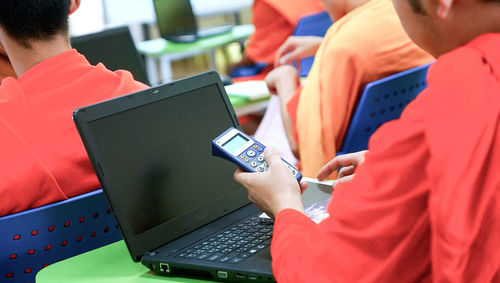 Midsection of boy holding calculator by laptop on desk in classroom