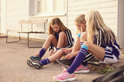 Girls sitting on footpath tying shoelaces