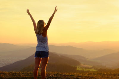 Rear view of woman standing on mountain during sunset