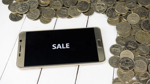 High angle view of sale text in smart phone by coins on table