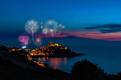 Firework display over sea against sky at night