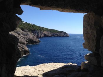 Rock formations by sea against clear blue sky