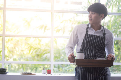 Man having drink while standing by window in cafe