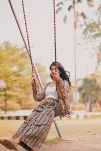 Side view of young woman sitting on swing at playground