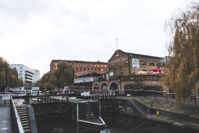 Bridge over river by buildings in city against sky