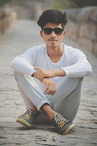 Portrait of young man wearing sunglasses while sitting on footpath
