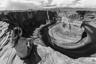 High angle view of woman sitting on cliff against sky