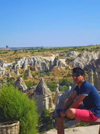 Man looking away while sitting on rocks at nevsehir against clear blue sky