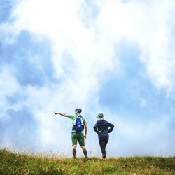 Rear view of friends standing on grassy field against cloudy sky