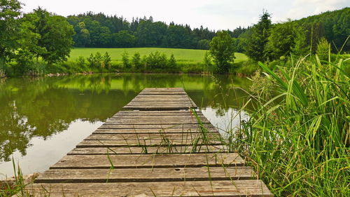 Wooden walkway by lake against sky