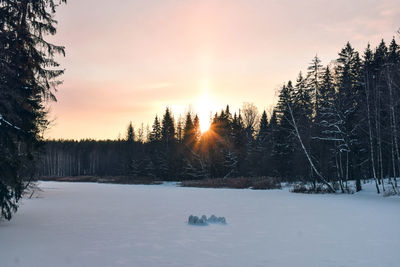 Snow covered field against sky during sunset