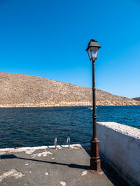 Street light by sea against clear blue sky