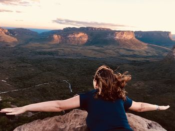 Rear view of woman standing on rock against sky