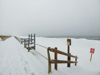 Snow covered railing by sea against sky