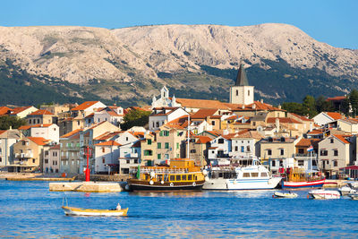 Boats in sea by townscape against mountain