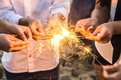 Midsection of people holding illuminated sparklers at night