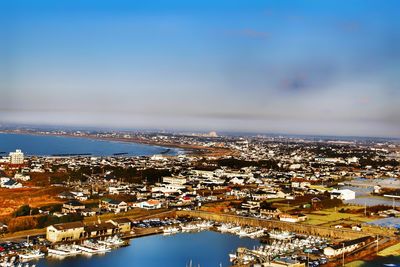 Aerial view of illuminated city by sea against sky