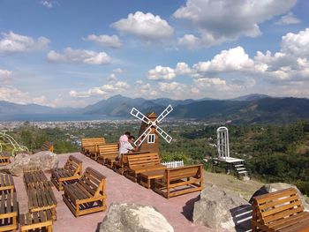 Men sitting on table by windmill against cloudy sky