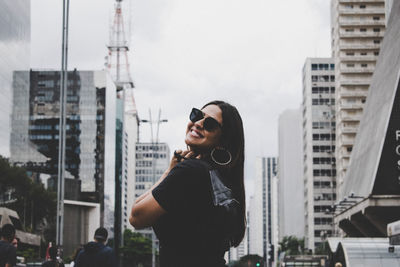 Young woman wearing sunglasses standing against buildings in city