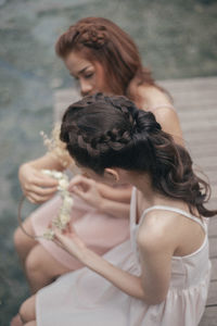 High angle view of young friends making tiara while sitting on jetty