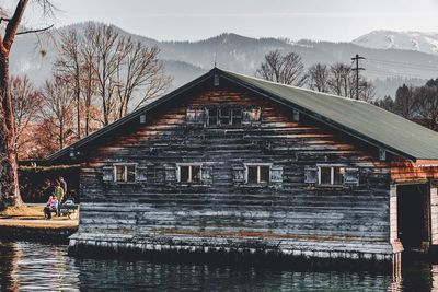 Group of people on house by lake against sky