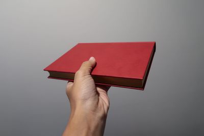 Close-up of hand holding book against gray background