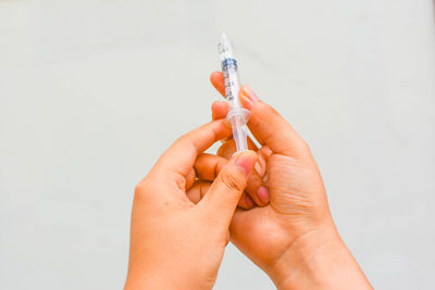 Cropped hands of woman holding syringe against wall