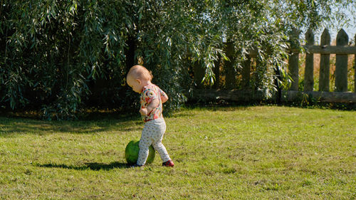Full length view of a little child kicks the ball on the grass first time in her life