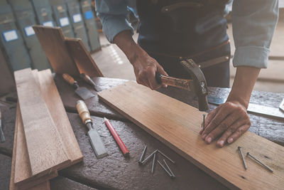 Midsection of carpenter hammering nail in plank at workshop