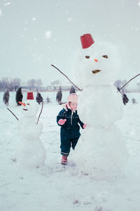 Full length of girl standing by snowman on field against sky