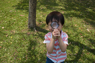 High angle view of boy holding magnifying glass while standing on field