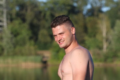 Portrait of shirtless man standing against trees in forest