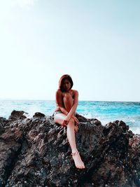 Woman sitting on rocks at beach against sky