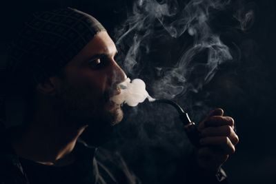 Close-up of man smoking against black background