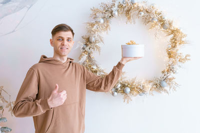 Happy young man holding gift box on background christmas wreath on background