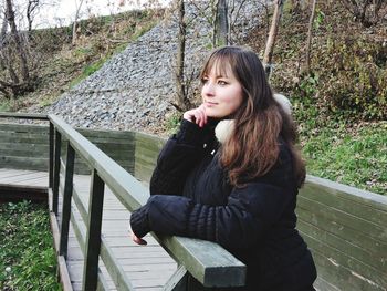 Portrait of young woman sitting on railing in park