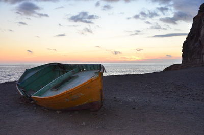 Abandoned boat on beach against sky during sunset