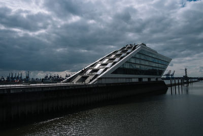 Footbridge over river in city against cloudy sky