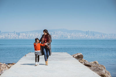 Full length of young woman standing at beach against clear sky